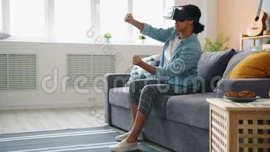 戴着vr眼镜的美国黑人女士正在<strong>家中</strong>享受着移动手臂和腿的驾驶游戏