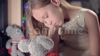 一个小悲伤失望的女孩坐在人造壁炉旁，在柔软的玩具旁边感到悲伤。 被宠坏的概念