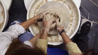 从浪漫情侣肮脏的双手上方拍摄的照片，他们一起在陶工轮上工作，一起雕刻陶罐