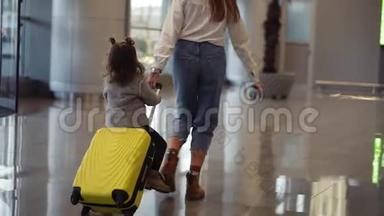 机场候机楼，年轻的无法辨认的母亲骑着她可爱的女儿在一个小黄色的手提箱。 妈妈是黄色的