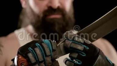 一个留着胡子的人，戴着黑色工作室的手套，手指沿着砍刀的刀刃。