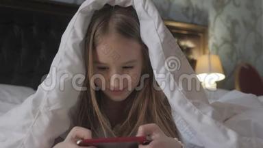 在黑暗的光线下，躺在床上的少女在<strong>社交网络</strong>上玩平板电脑。 特写小<strong>女孩</strong>看视频的画面