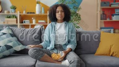 恐怖的非裔美国女孩在电视上看恐怖片吃零食的肖像