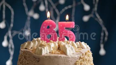 生日蛋糕，上面有65号粉红色燃烧的蜡烛，在蓝色的背景上。 蜡烛吹灭了。 慢<strong>速运</strong>动和特写镜头