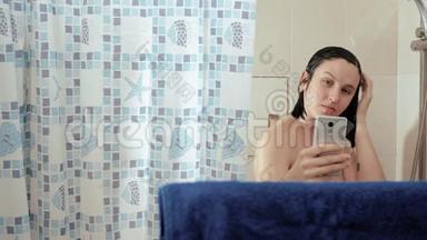 淋浴女孩在智能手机中使用互联网，阅读新闻社交网络。 她的头上涌着水。 慢动作