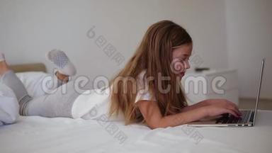 长发欧洲女孩在<strong>笔记本电脑</strong>上打字。 微笑的小女孩带着兴趣，看着<strong>笔记本电脑</strong>，躺在床上。 侧视图