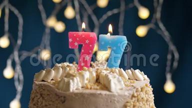 生日蛋糕上有77个数字的粉红色燃烧蜡烛在蓝色的背景上。 蜡烛吹灭了。 慢<strong>速运</strong>动和特写镜头