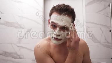 年轻帅哥的肖像正在涂上新鲜的白色厚厚的面具，并在脸上擦洗。 天然有机化妆品