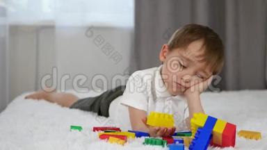 快乐快乐的男孩躺在床上玩彩色积木。 一个孩子从meccano那里建立起来。