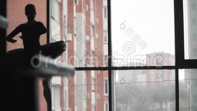 剪影。 芭蕾舞演员穿着黑色的芭蕾舞裙在窗户和城市的背景下跳舞。 慢动作。 静止的框架
