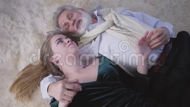 快乐微笑的白人夫妇的肖像，年龄差异，躺在柔软的地毯上聊天。 最爱的人的视角