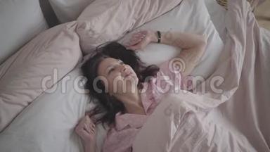正面的成年白种人女人的俯视图早上躺在床上对着镜头微笑。 快乐的肖像