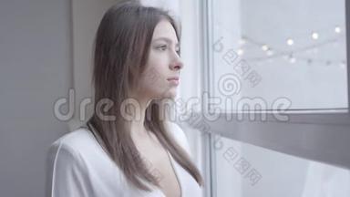 一位深谋远虑、深褐色眼睛的白种人女人的特写镜头，<strong>看着窗外</strong>的家。 可爱的女孩醒来
