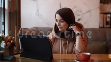 一位穿着休闲服的年轻美女正在一家舒适的咖啡馆使用数码平板电脑。