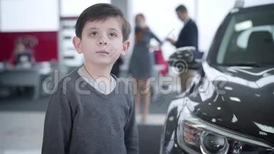 一个可爱的白人小男孩站在新车旁，<strong>回头</strong>看着父母和商人交谈。可爱的