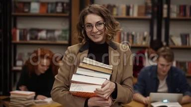 吸引<strong>人</strong>的欧洲女学生拿着书在高中<strong>图书馆</strong>微笑着看相机的肖像。 教育
