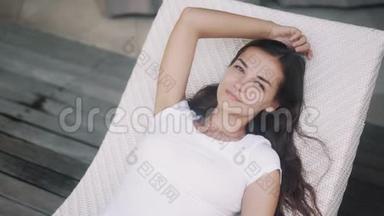 身穿白色t恤的女人躺在靠近游泳池的日光浴床上，放松<strong>身心</strong>，享受假期