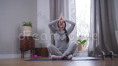 棕色皮肤的白人女人坐在瑜伽垫上举起双手，把它们放在一起。 冥想