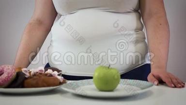 无法辨认的白种人成年女人站在<strong>桌子上</strong>，<strong>桌子上放</strong>着糖果和苹果。 肥胖女孩选择