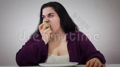 沮丧的年轻白人胖女孩吃苹果。 胖女人把水果放在一边，看着远处。 自我控制，节食