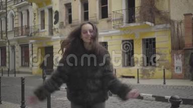 穿着毛皮外套和太阳镜的快乐时尚女孩在城市街道上玩得开心的肖像。 快乐的年轻女子跳舞
