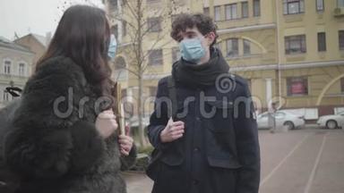 两名戴防护面罩的大学生在城市街道上交谈。 认真负责的男孩和女孩在户外聚会