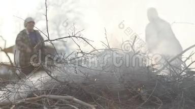 一群干树枝在前台燃烧，这是一对高种高加索农民在后台控制着火势