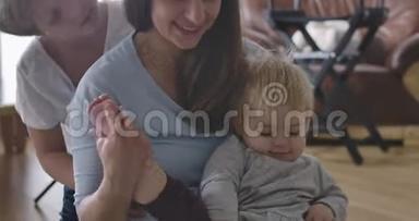 年轻的高加索母亲坐在地板上，小女儿作为她的大儿子亲吻她的脸颊。 快乐的女人