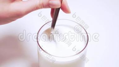 这位女士`用勺子在一个玻璃杯里用圆形的动作搅拌农场酸奶。 透明玻璃杯中的新鲜豆浆