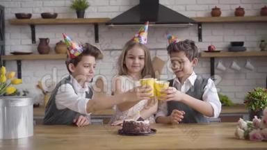 快乐的女孩和两个相同的男孩在生日聚会上<strong>碰杯</strong>喝茶。 双胞胎兄弟<strong>庆祝</strong>节日