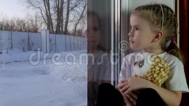 一个拿<strong>着</strong>玩具的小女孩坐在窗台上<strong>看着窗外</strong>