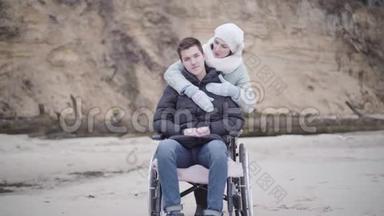 微笑的白种人女人拥抱轮椅上的残疾人的肖像。 年轻残疾男孩和看起来很嫩