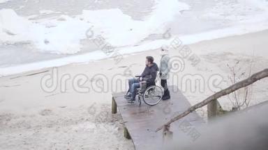 坐在轮椅上的白种人残疾男孩和站在码头上看着结冰的河流的无效投标。 青年<strong>残疾人</strong>