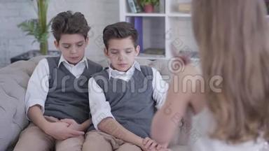 无法辨认的小白种人黑发女孩颤抖的手指，骂<strong>双胞胎兄弟</strong>坐在沙发上。 优雅的男孩