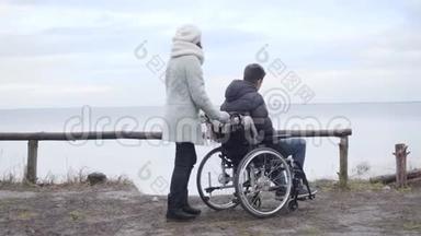 年轻的积极白人妇女停止轮椅与残疾男孩在河岸和指向。 母亲开支