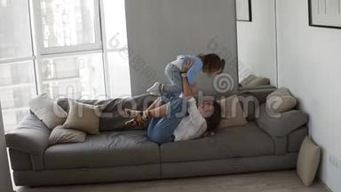 幸福的家庭母亲和孩子女儿一起在沙发上玩得开心。 年轻女子挠痒痒，引进来