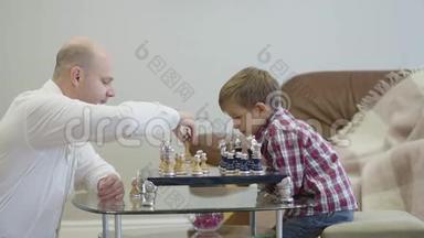 侧面看白人男子穿着白色衬衫坐在<strong>棋盘</strong>前和聪明的儿子玩。 可爱的聪明男孩