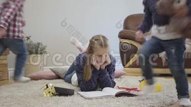两个开朗的白人孩子在姐姐<strong>身边</strong>跑来跑去，躺在柔软的地毯上看书。 少女想要