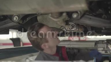 白种人维修工程师出现在汽车下面。 汽车修理工在修理厂检查车底