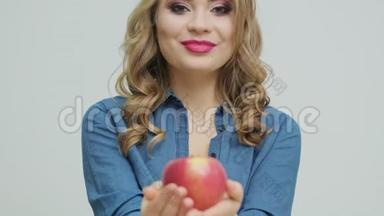可爱的女人在一张桌子上拿着一个苹果，背景是水果和蔬菜。