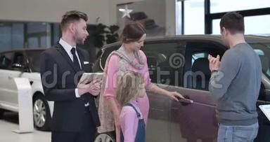 年轻的高加索家庭在汽车陈列室挑选新汽车。 男人，女人，还有小可爱的女孩