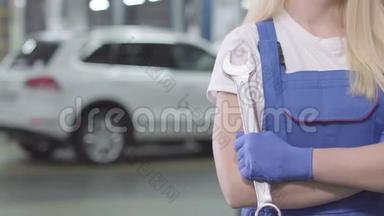 不可辨认的白种人女人穿着工作长袍和手套交叉手拿扳手。 年轻女汽车修理工
