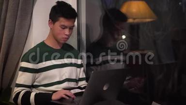 年轻的亚洲男孩在笔记本电脑上打字和晚上<strong>看窗外</strong>的肖像。 帅哥大学生