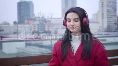自信的白人女孩戴着红色外套和手套戴着耳机的肖像，就像坐在城市里的小雨或