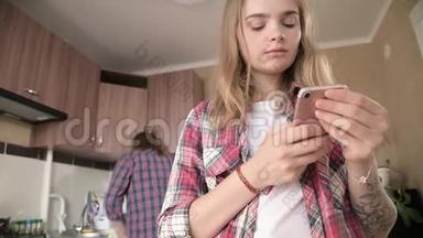 年轻的夫妻在厨房里。 一个有纹身的女孩在手机上给她的<strong>爱人</strong>写了一条信息