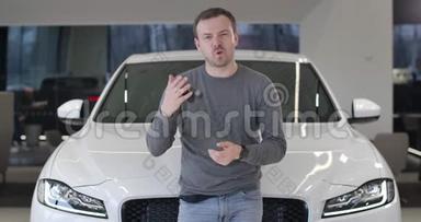 年轻的白人男子站在新的白色汽车和吹嘘汽车钥匙。 汽车幸福车主画像