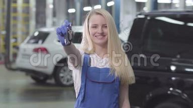 带着微笑的金发白种人女人的肖像，她展示了汽车钥匙的镜头。 年轻的女汽车修理工对她的工作很满意