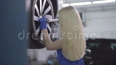 侧面观看金发白种人妇女拧紧车轮<strong>螺丝</strong>。 在修理厂工作的年轻女<strong>汽车</strong>修理工