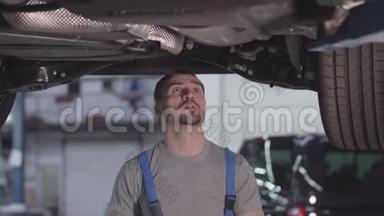 白种人<strong>汽车</strong>机械师站在车下检查<strong>螺丝</strong>的肖像。 在修理厂工作的英俊的年轻人