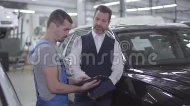 自信的白种人汽车机械师在平板电脑屏幕上向客户展示一些东西的肖像。 专业咨询